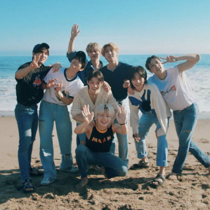 a group of young people standing on top of a sandy beach next to the ocean