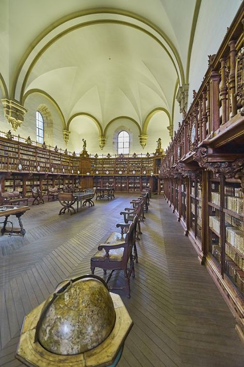 an empty library with benches and tables in the foreground, surrounded by bookshelves