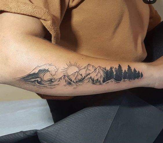 a man's arm with a mountain and pine tree tattoo on the left forearm