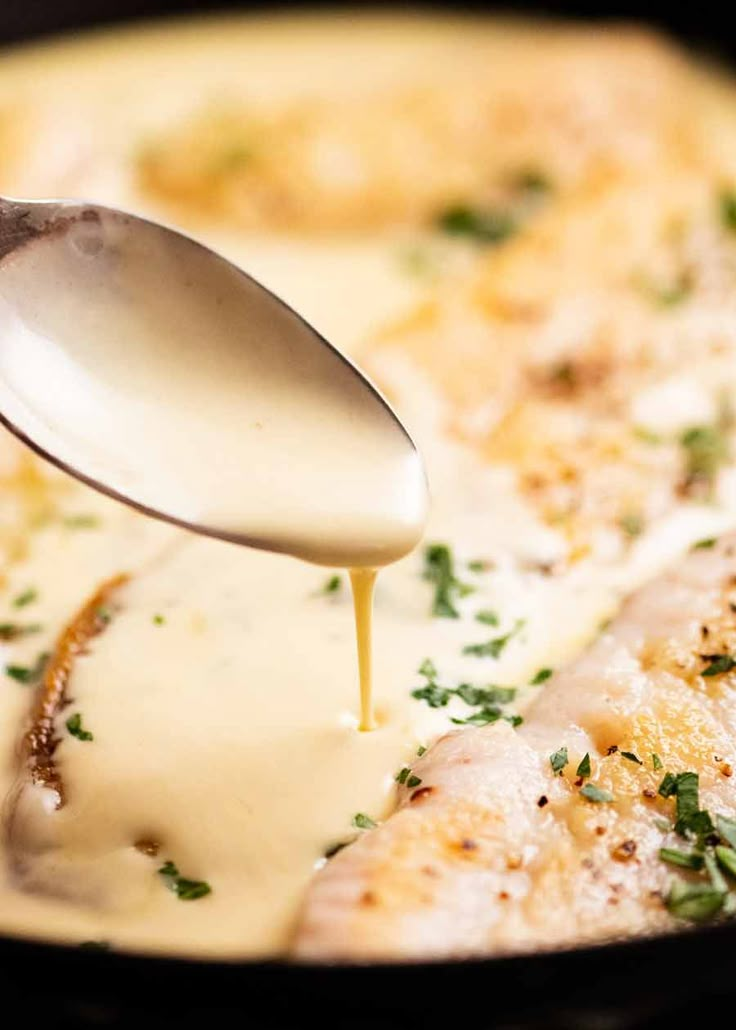 a spoon is pouring sauce on some food in a skillet with cheese and herbs