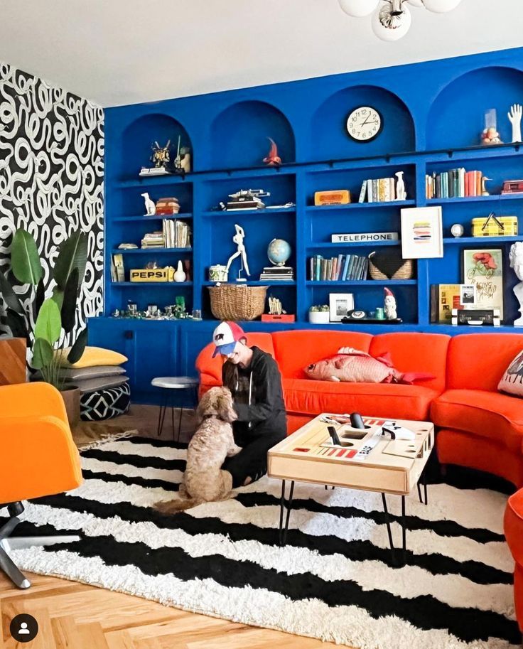 a living room with blue walls and orange couches in the corner, while a dog sits on a black and white rug