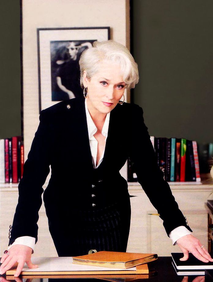 an older woman in a black suit leaning over a table with a book on it