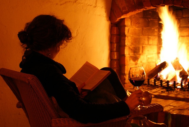 a woman sitting in a chair reading a book and holding a glass of red wine