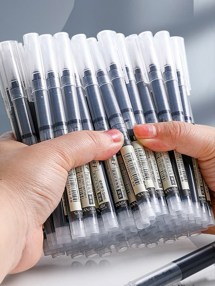 a person holding a bunch of pens in their hand next to some other pen holders