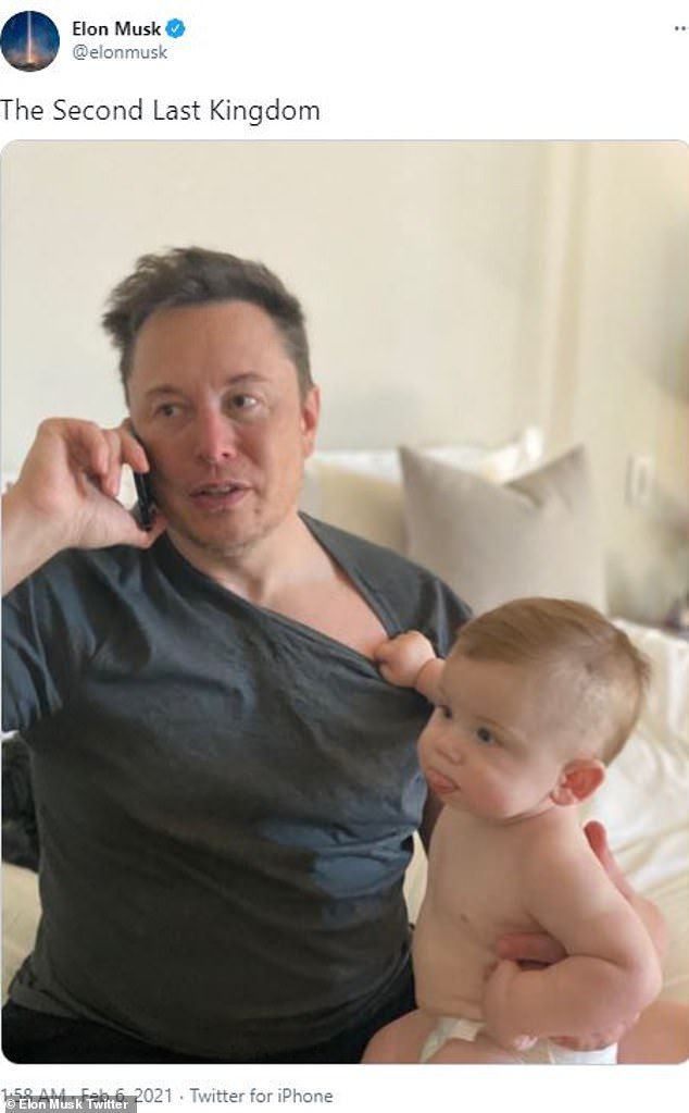 a man sitting on a bed holding a baby and talking on a cell phone while he holds his thumb up to his ear