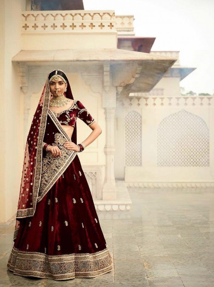 a woman in a red and gold bridal gown standing on a stone floor with her hands on her hips