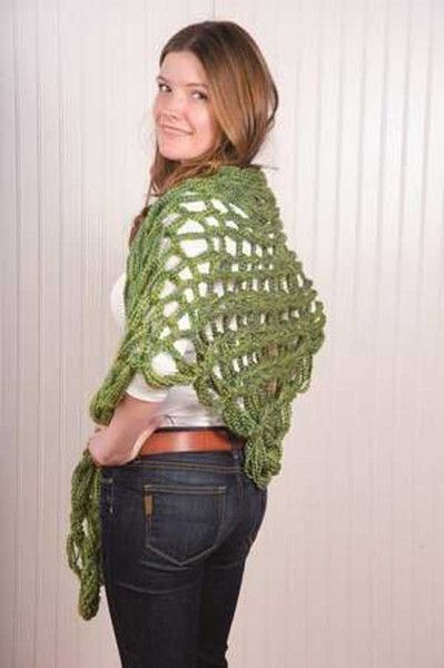 a woman standing in front of a wall wearing a green crocheted shawl