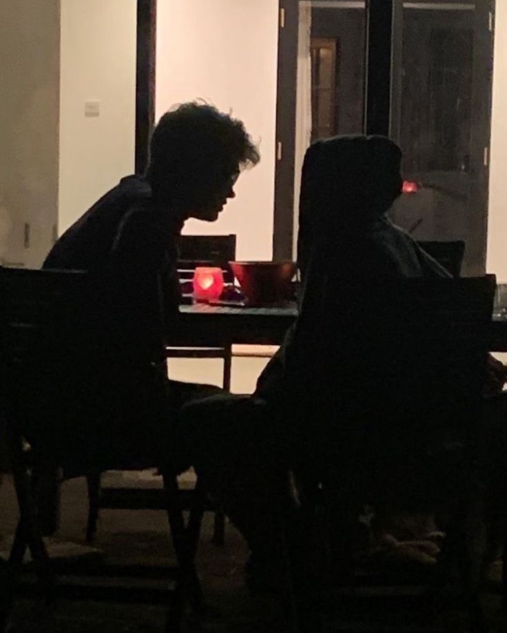 two people sitting at a table in front of a window with a red light on it