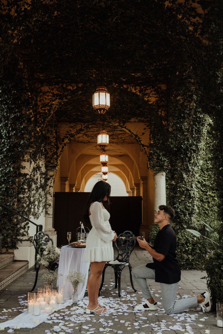 a man kneeling down next to a woman in front of a table with flowers on it