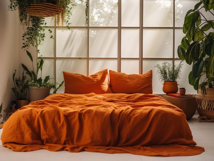 a bed with orange sheets and pillows next to potted plants