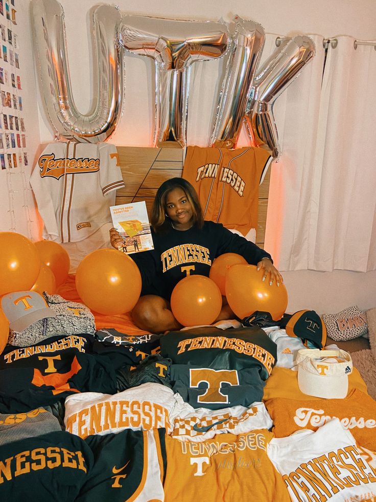 a woman sitting on top of a bed surrounded by orange and white balloons in the shape of letters