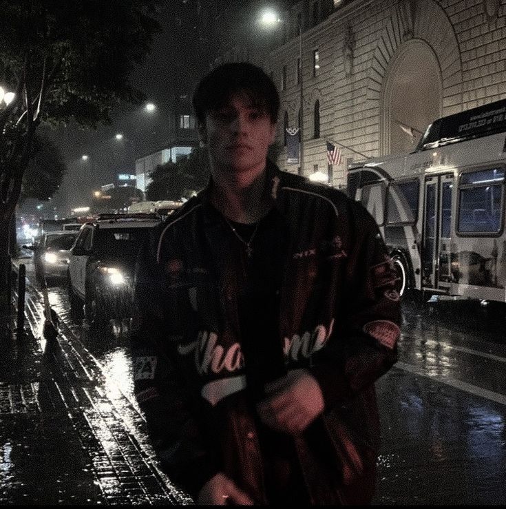 a man standing in the rain on a city street at night with his umbrella up