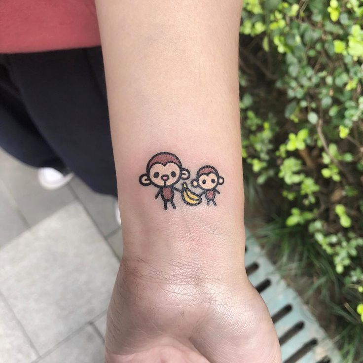 a small tattoo on the wrist of a person with two monkeys holding bananas in their hands