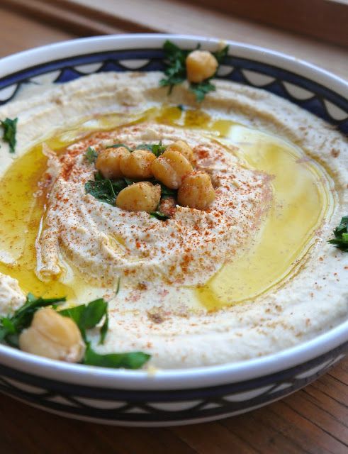 a bowl filled with hummus and garnish on top of a wooden table