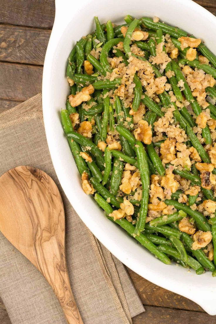 green beans with breadcrumbs in a white dish next to a wooden spoon