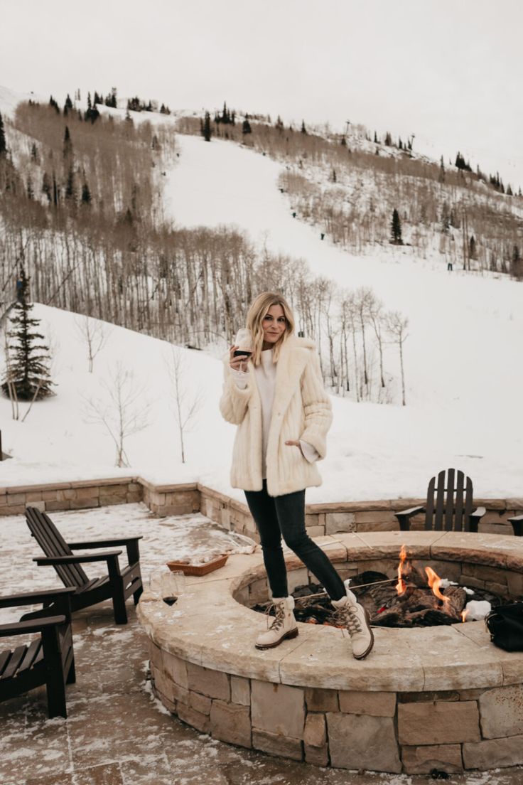 a woman standing in front of a fire pit on top of a snow covered slope