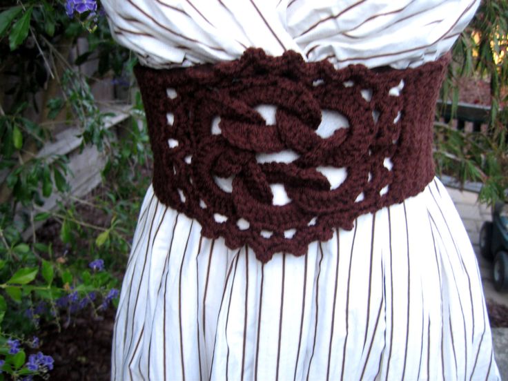 a woman wearing a brown belt with white stripes on it and flowers in the background