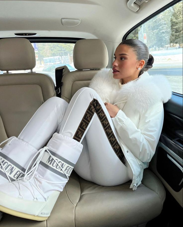 a woman sitting in the back seat of a car wearing white boots and fur collar