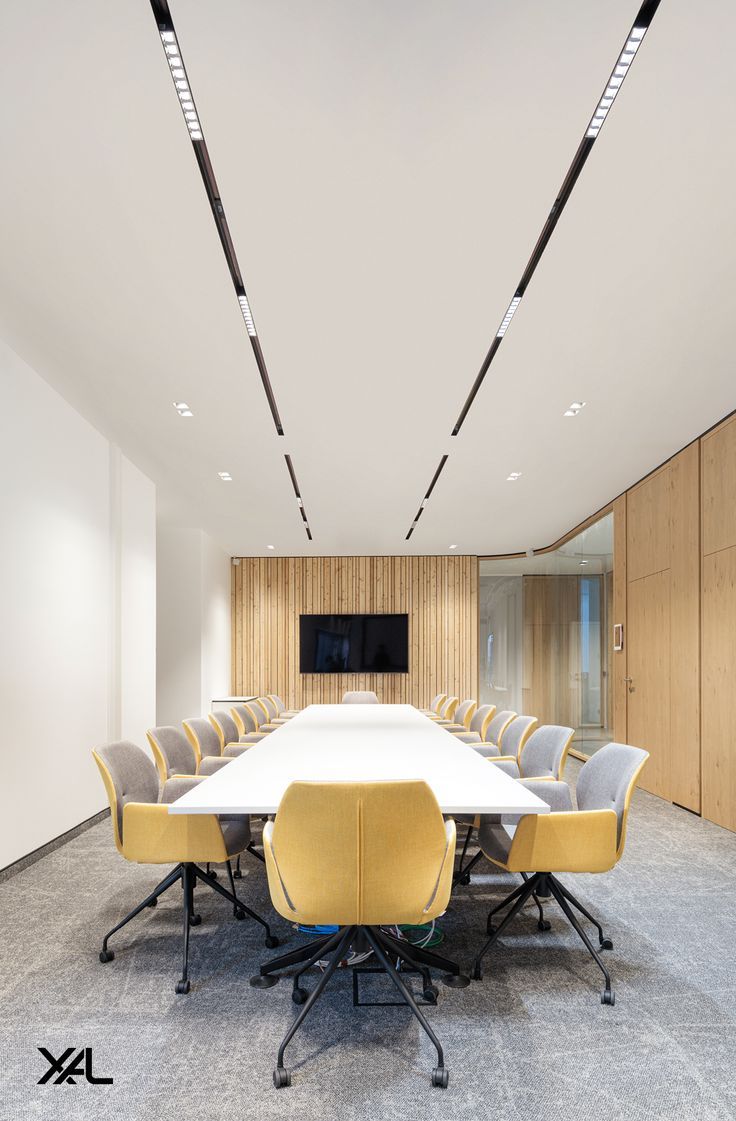 an empty conference room with yellow chairs and a white table in front of a flat screen tv