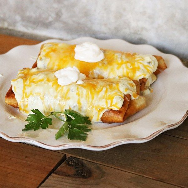 two enchiladas on a white plate topped with sour cream and parsley