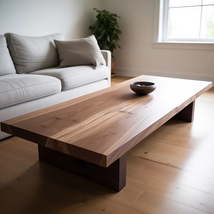 a wooden table with a bowl on it in front of a white couch and window