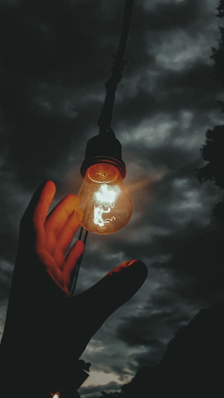 a hand holding an old fashioned light bulb in front of a dark sky with clouds