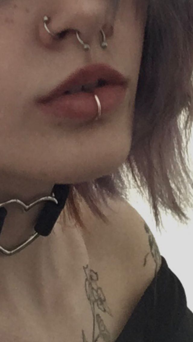 a woman with piercings on her nose wearing a black choker and silver hoop earrings