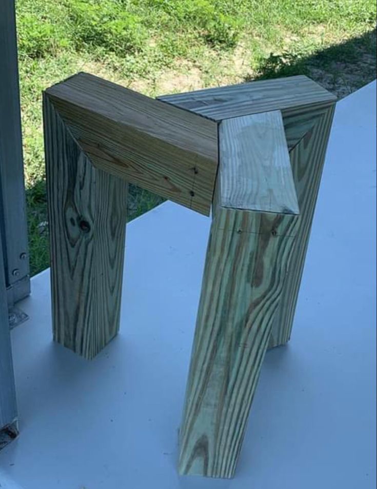 a wooden stool sitting on top of a white table next to a grass covered field