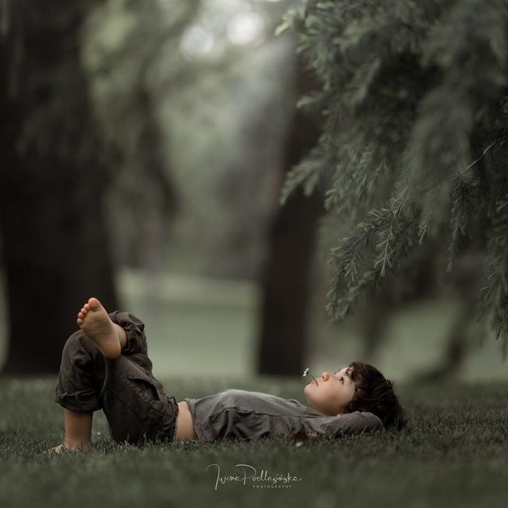 a young boy laying on the grass in front of some trees