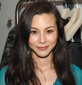 a woman standing in front of a rack of clothes and looking at the camera with a smile on her face