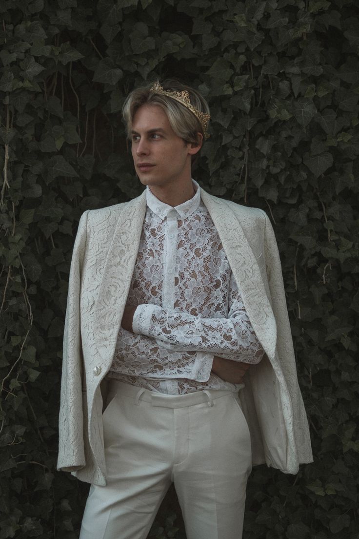 a man wearing a white suit with a crown on his head standing in front of a green wall