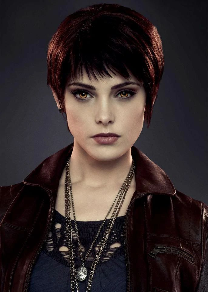 a woman with short hair wearing a leather jacket and necklaces is looking at the camera