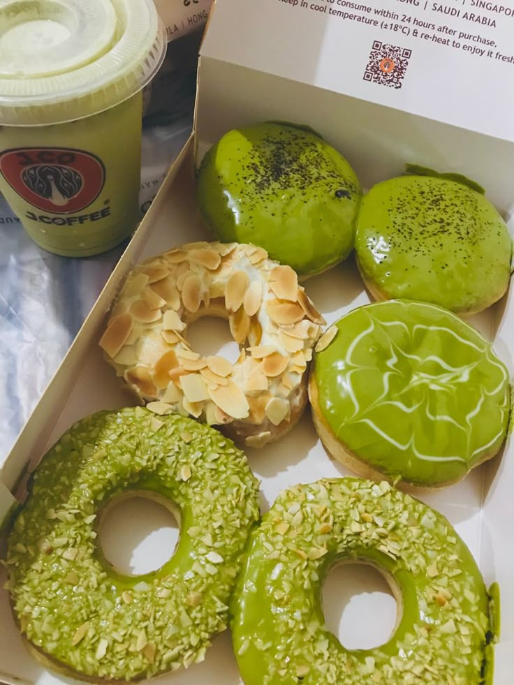 a box filled with assorted green donuts next to a cup of yogurt