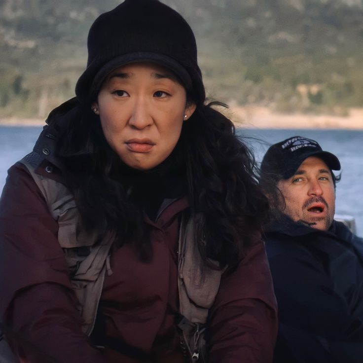 two people sitting next to each other in front of the ocean and one person wearing a black hat