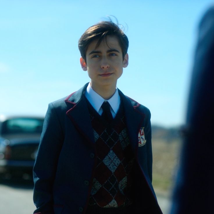 a young man wearing a vest and tie standing in front of a car