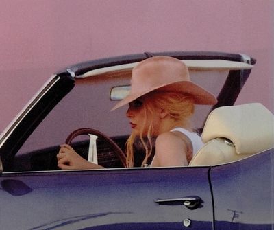 a woman sitting in the driver's seat of a blue convertible with a hat on