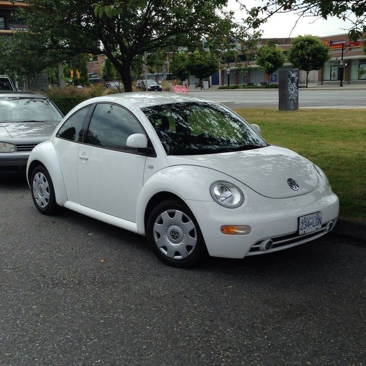 a white car is parked on the side of the road next to another car and some trees