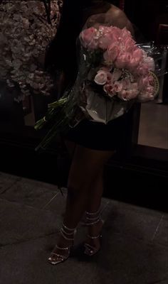 a woman is standing on the sidewalk holding flowers