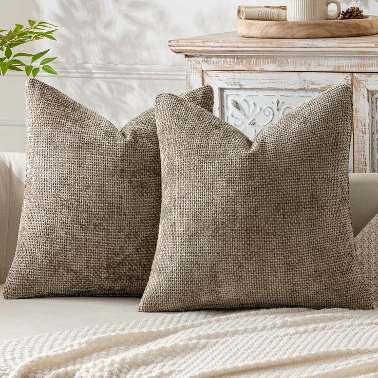 two pillows sitting on top of a white couch next to a table with a potted plant