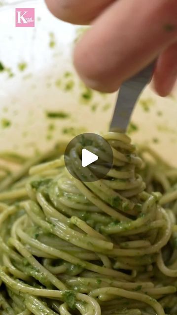 someone is using a fork to stir green pasta in a bowl with pesto on top