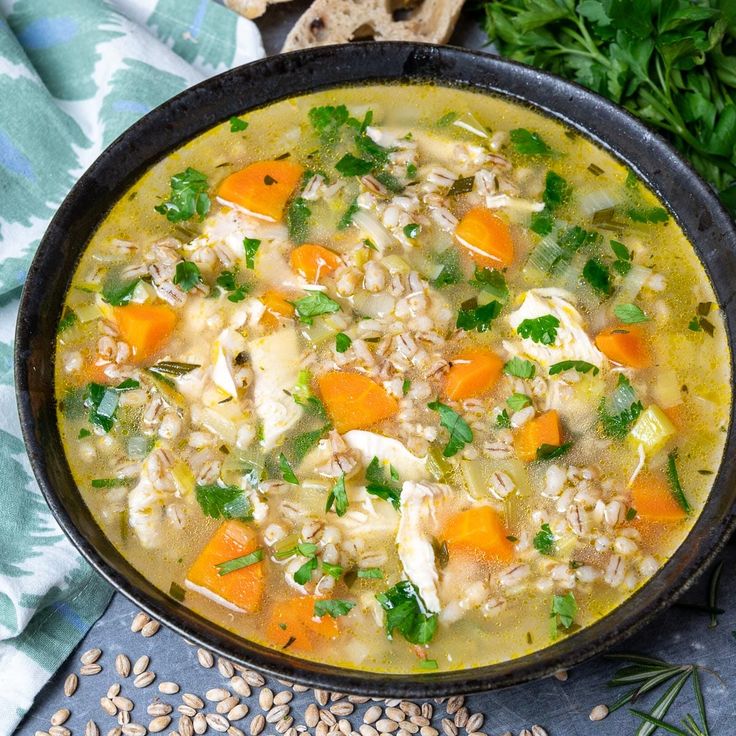 a bowl filled with chicken and rice soup next to bread on top of a table