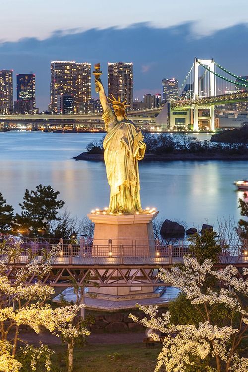 the statue of liberty is lit up at night in front of the bay bridge and city lights