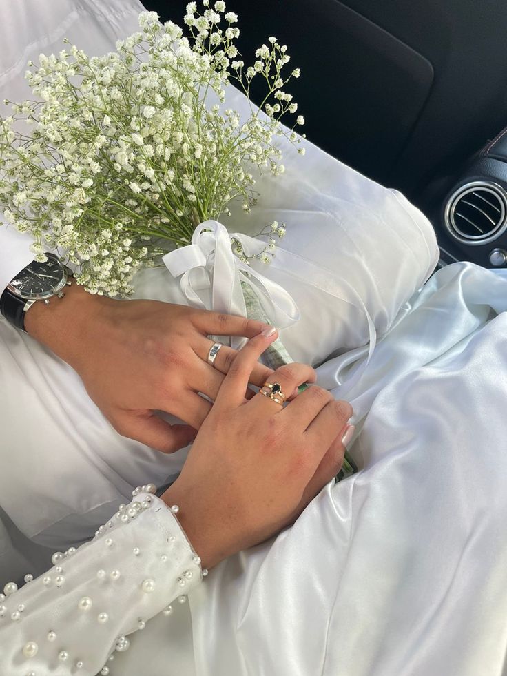 a person in a car with flowers and wedding rings on their hands, holding the bouquet