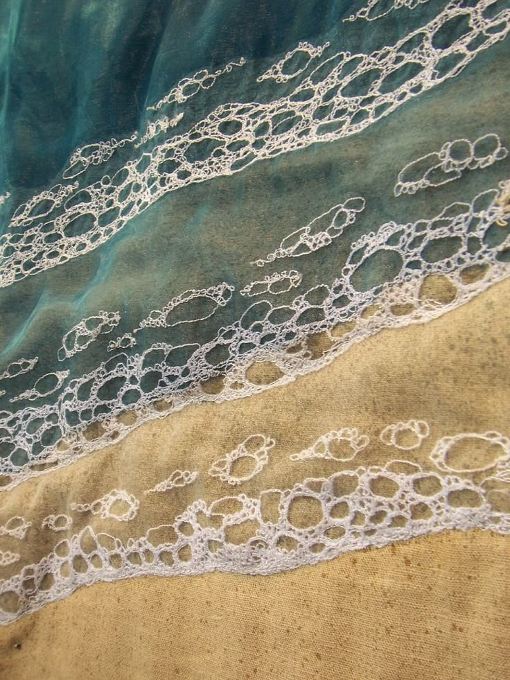 an aerial view of the ocean and sand with white lace on it's edges