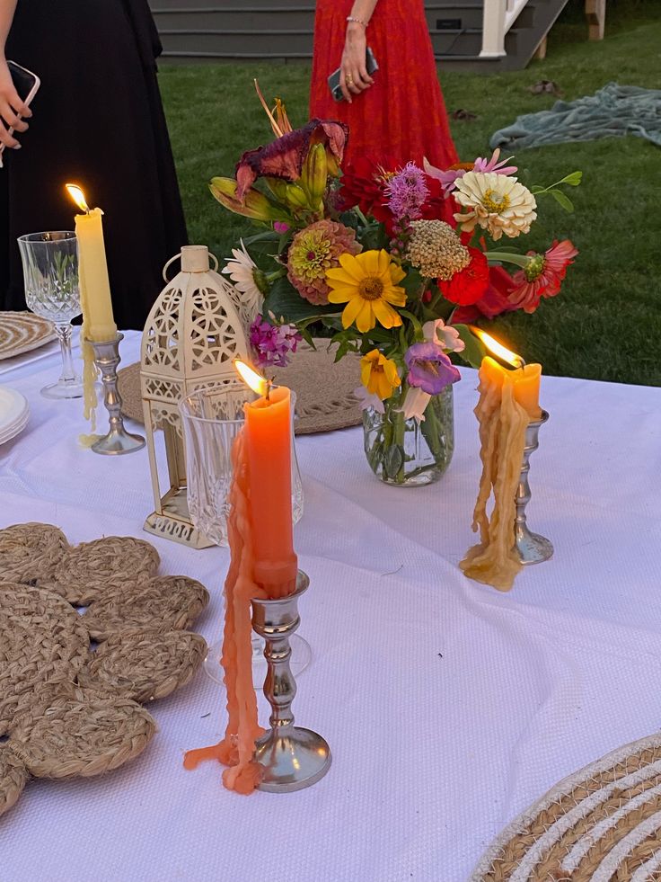 a table with candles, cookies and flowers on it in front of two women standing next to each other