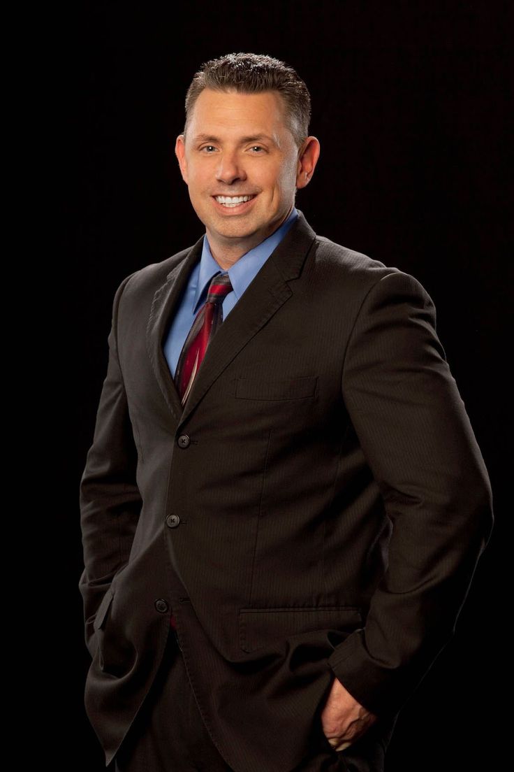 a man in a suit and tie standing with his hands in his pockets, smiling at the camera