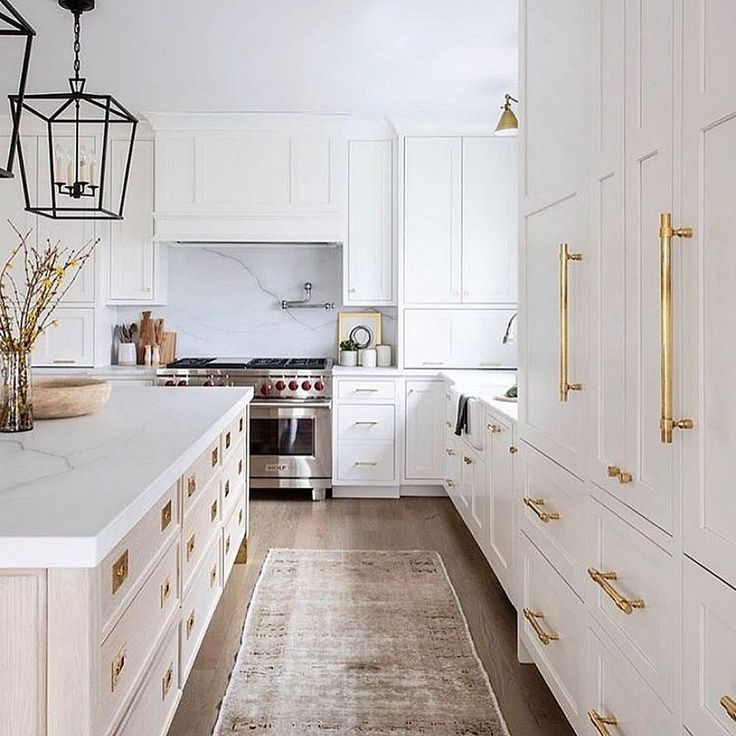 a large kitchen with white cabinets and gold pulls on the drawers, along with an area rug