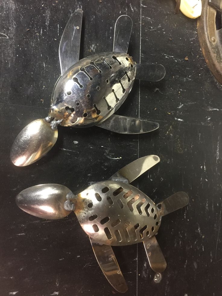 two metal sea turtle shaped utensils sitting on top of a black table next to each other