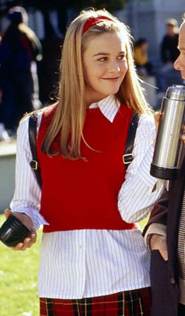 a woman in a red shirt and plaid skirt holding a coffee cup while standing next to a man