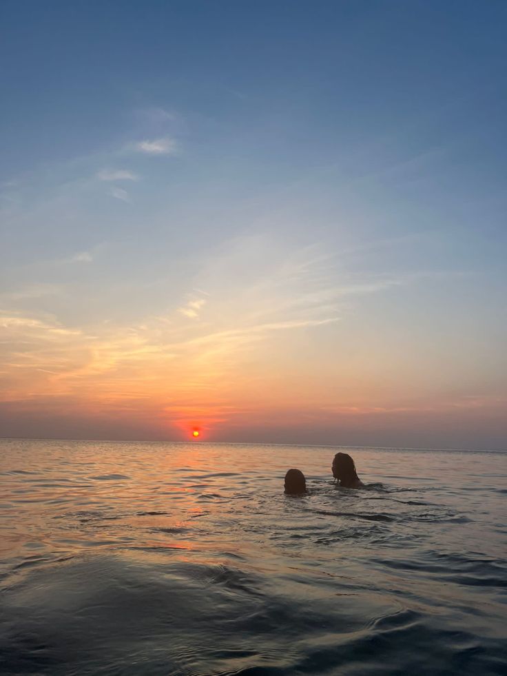 two people swimming in the ocean at sunset